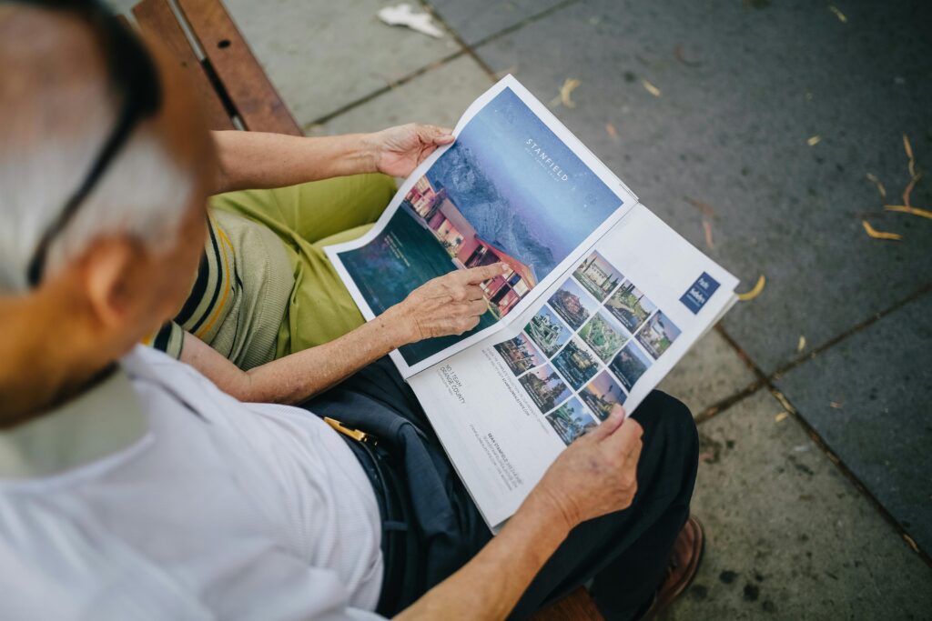 An elderly couple sitting outdoors on a bench reading a magazine together, sharing a moment.
